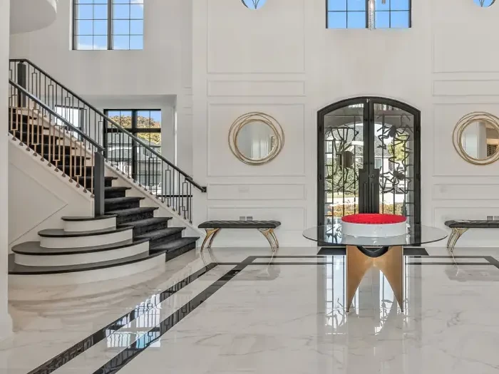 Two-story entry hall with a curved staircase, arched windows, a crystal chandelier and white marble floors with a black border