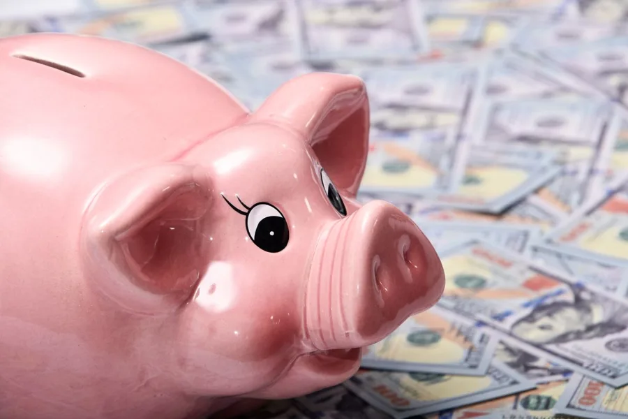Pink piggy bank on a spread of hundred-dollar bills