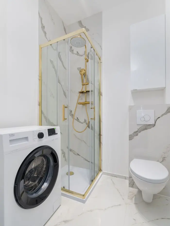 Compact ADU bathroom with walk-in shower, tiled walls and in-unit laundry